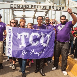  A group ɫ students walks across the Edmund Pettus Bridge in Selma, Alabama. They hold a ɫ flag and several students make the wo-fingered Go Frogs hand gesture.