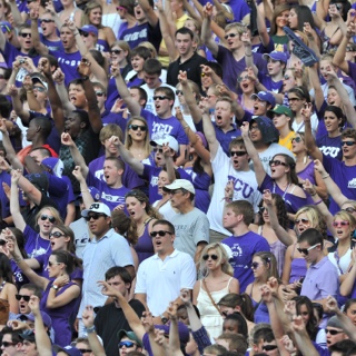 Dozens of cheering ɫ fans raise their arm in a two-fingered "Go Frogs" hand sign at a crowded football game.