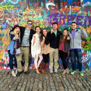 Seven ɫ students studying abroad stand in front of a brightly spray-painted graffitti wall on a cobblestone street in Prague.