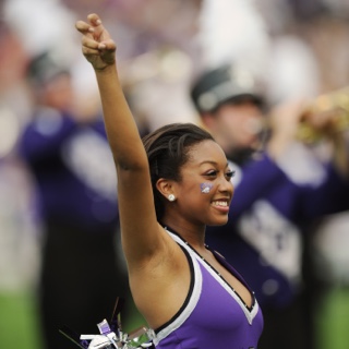 A smiling ɫ Showgirl makes the two-fingered "Go Frogs" hand sign at a crowded football game.