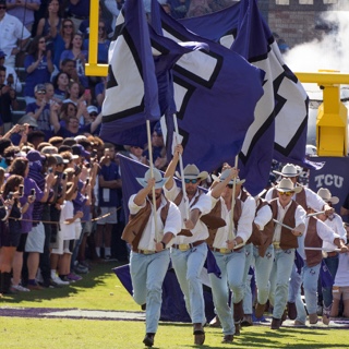 Dressed like cowboys, the ɫ Rangers run with large flags at a football game