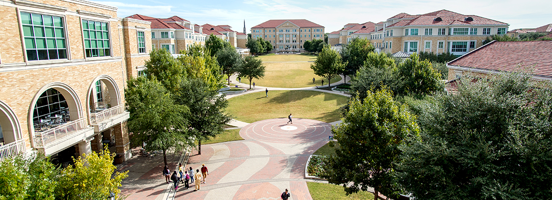 High up view of the ɫ campus commons with scattered groups of pedestrians. Frog Fountain is visible in the distance and a huge horned frog logo can be seen on the brick walkway