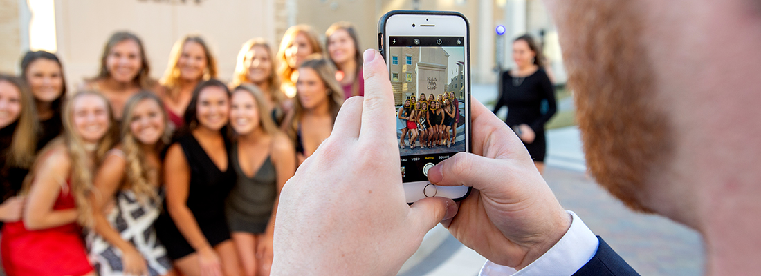 A young man uses a cell phone to photograph a group of smiling sorority girls before a party in the Greek Village at ɫ.