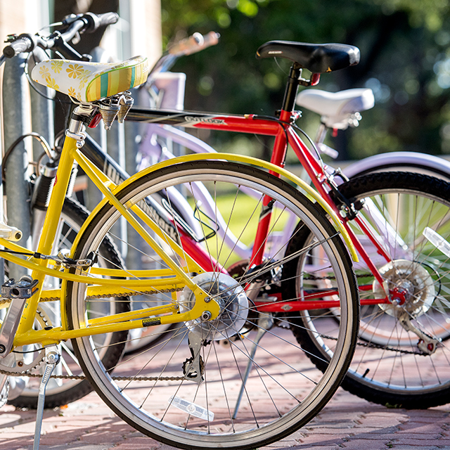 Close up of a bicycle rack on the ɫ campus with pink, red, and yellow bikes