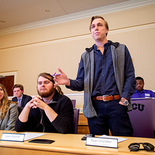 A male student stands to speak at a ɫ student government meeting in the chambers of the student union.